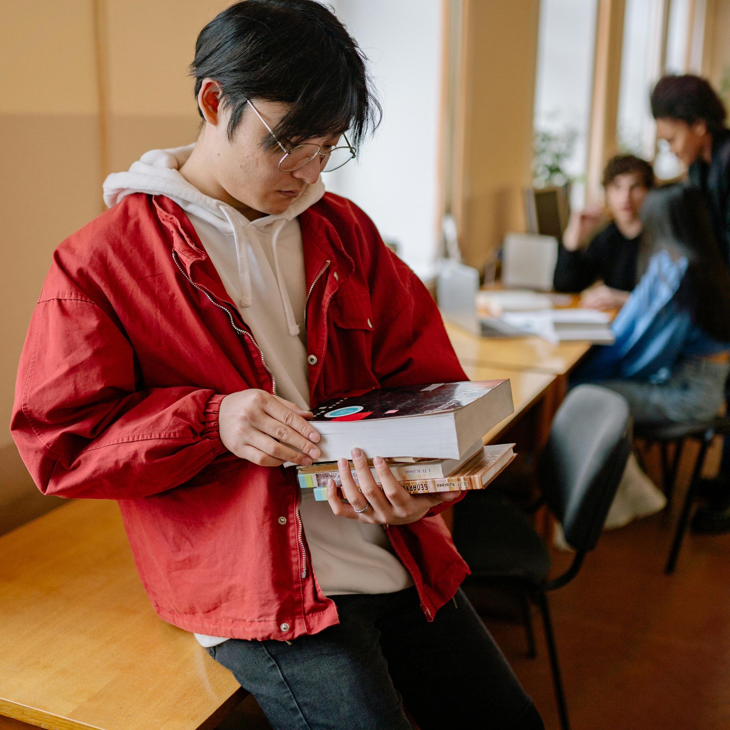 A young man wearing a red jacket quietly reads books in a serene library atmosphere.